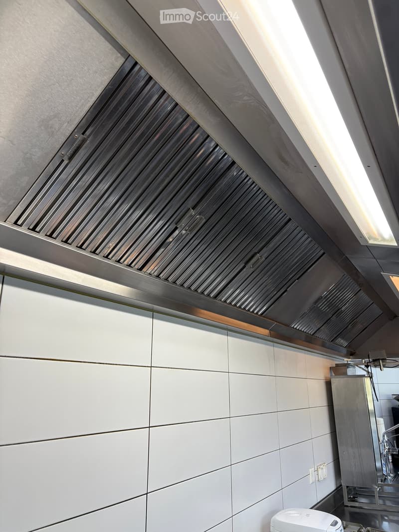 Modern kitchen with stainless steel range hood and white tiled backsplash.