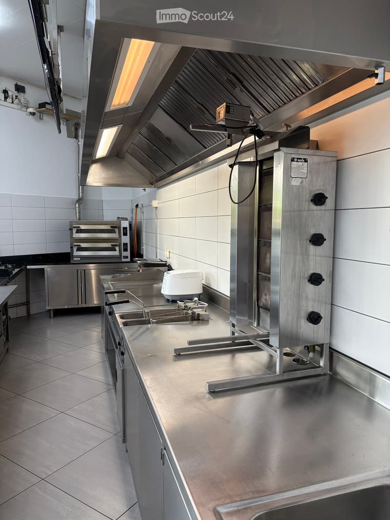 Commercial kitchen with stainless steel surfaces, oven, fryer, sink, and counter.
