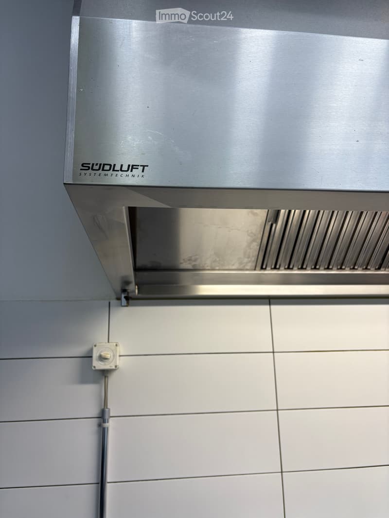 Stainless steel range hood mounted above a tiled wall, with a control knob visible below.