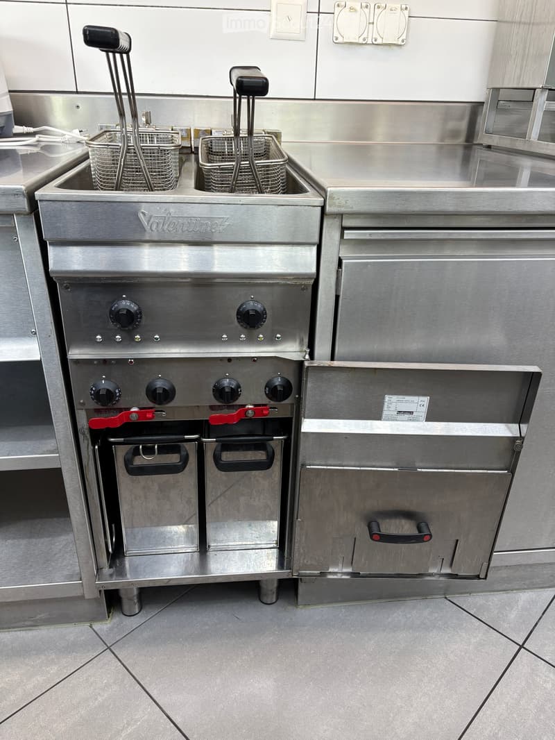Stainless steel commercial kitchen with a fryer, two baskets, and an oven, all mounted on a stainless steel countertop.