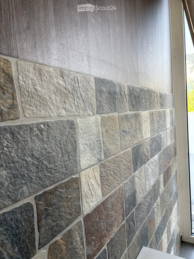 Empty room with a stone wall and a grey textured upper section, featuring a window frame on the right side.