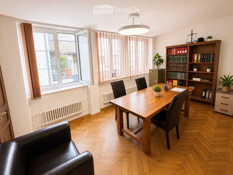 Well-lit room with wooden flooring, large windows with curtains, a leather sofa, a wooden desk with chairs, a bookshelf filled with books and plants, and a hanging lamp.