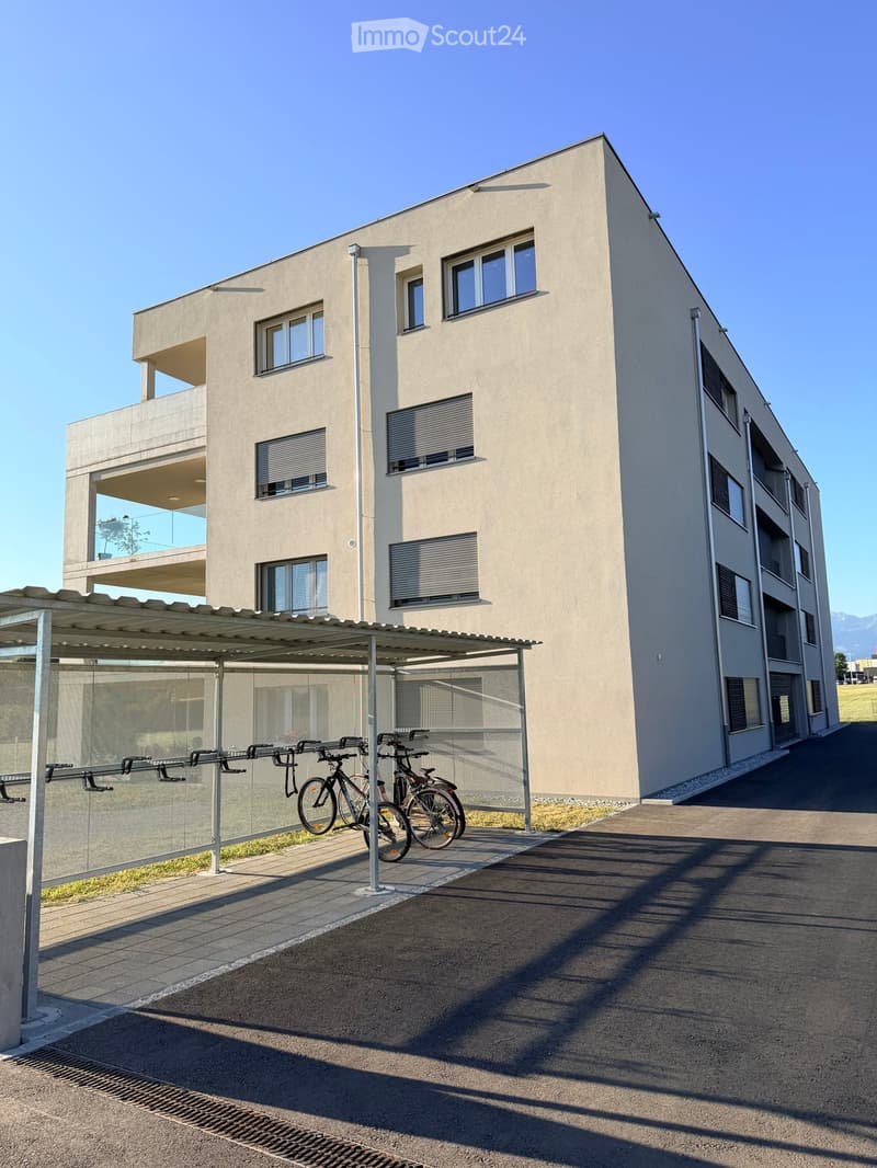 Modern multi-story building with large windows, balconies, and a covered bike parking area.