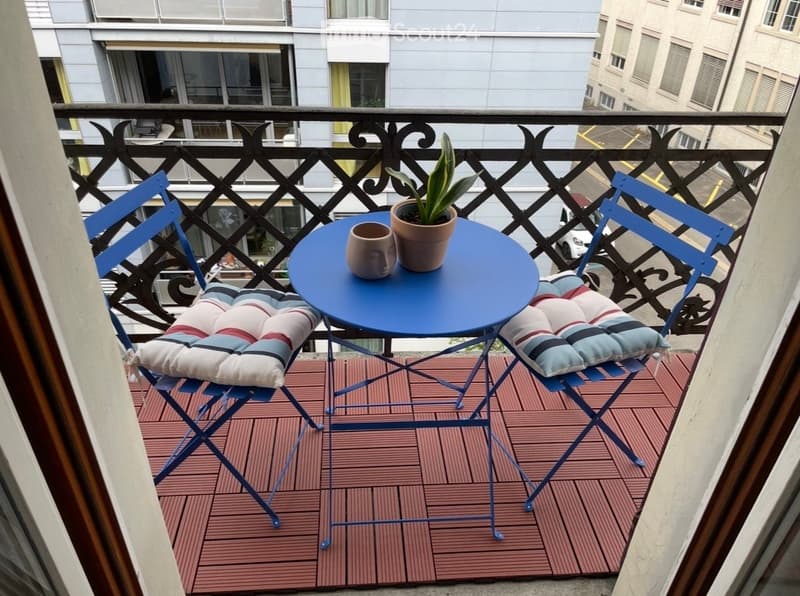 Balcony with a small round blue table, two blue chairs with striped cushions, a potted plant, and a cup on the table.