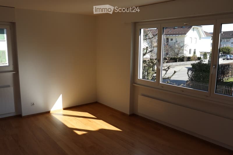 Empty room with wooden flooring, large windows, radiators, and natural light. No furniture or equipment present.