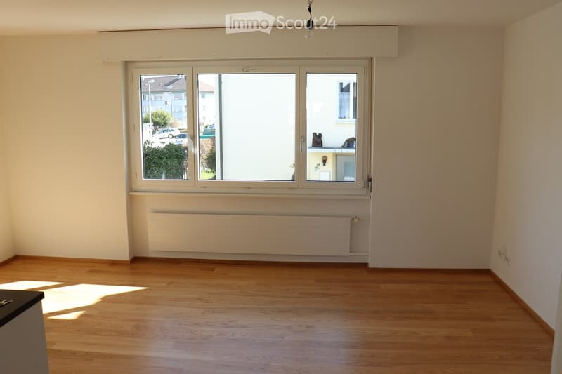 Empty room with wooden flooring, large window, radiator, and natural light. No furniture or equipment present.