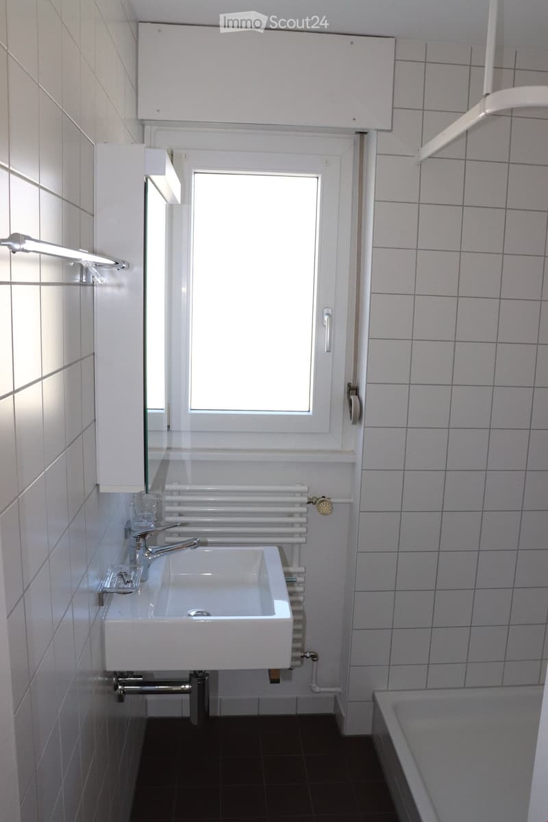 Modern bathroom with white tiles, a sink with a chrome faucet, a radiator, a mirror, and a bathtub.
