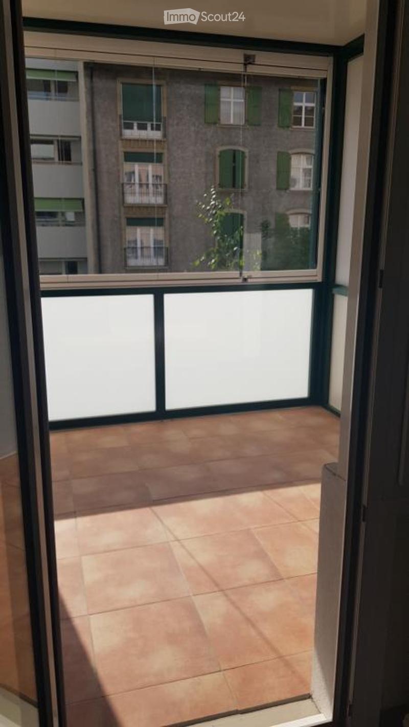 Balcony with tiled floor, large window offering a view of neighboring buildings and greenery.