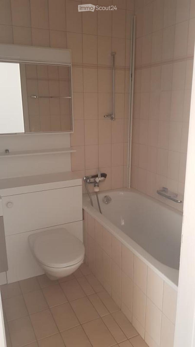 Modern bathroom with a white toilet, bathtub, mirror cabinet, and tiled walls and floor.