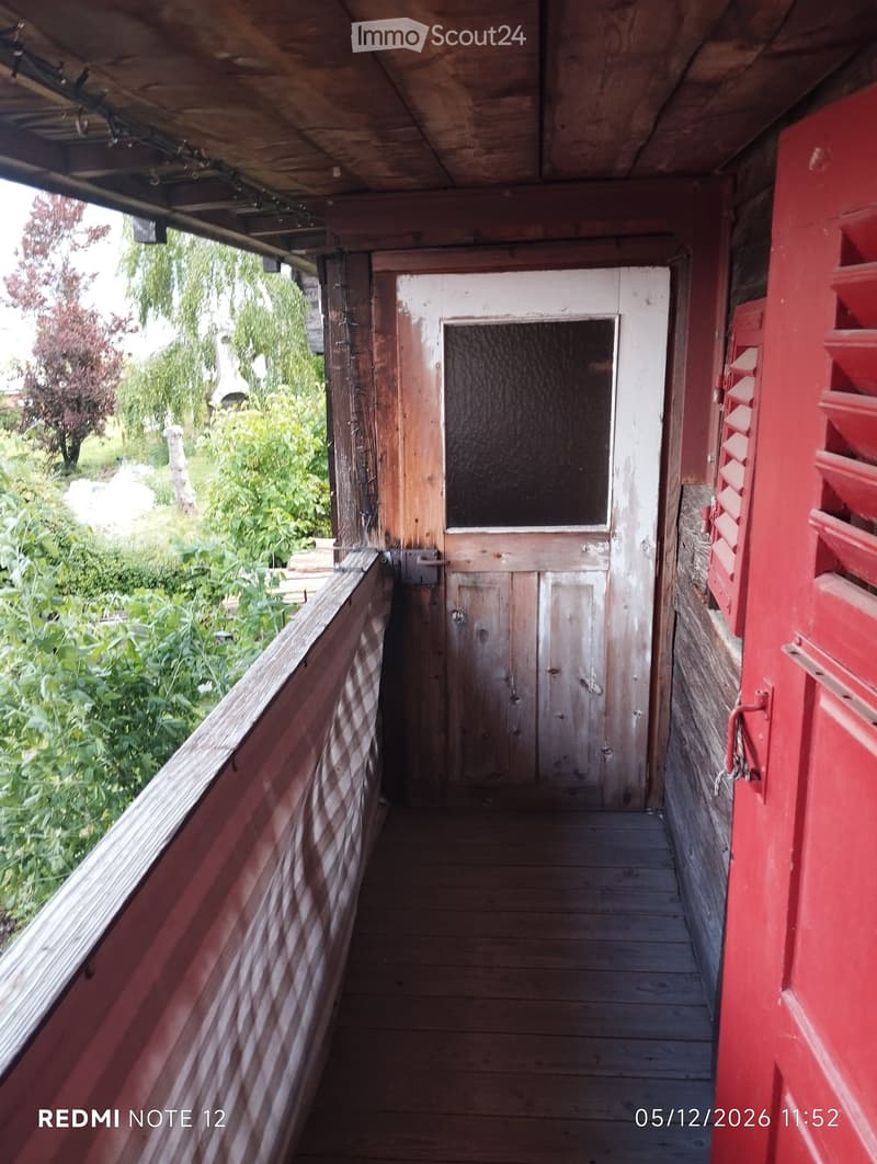 Wooden balcony with red railings, leading to a wooden door with a frosted glass panel.