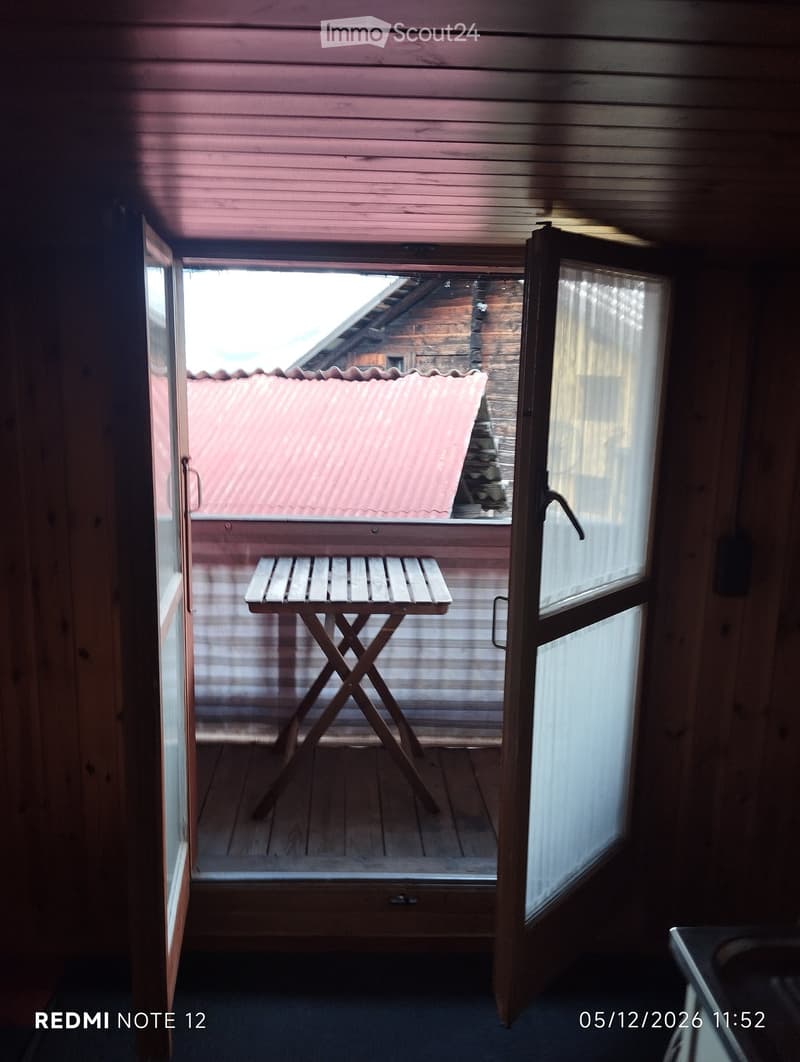 Wooden balcony with a small table, overlooking a wooden-roofed structure and a stone chimney.