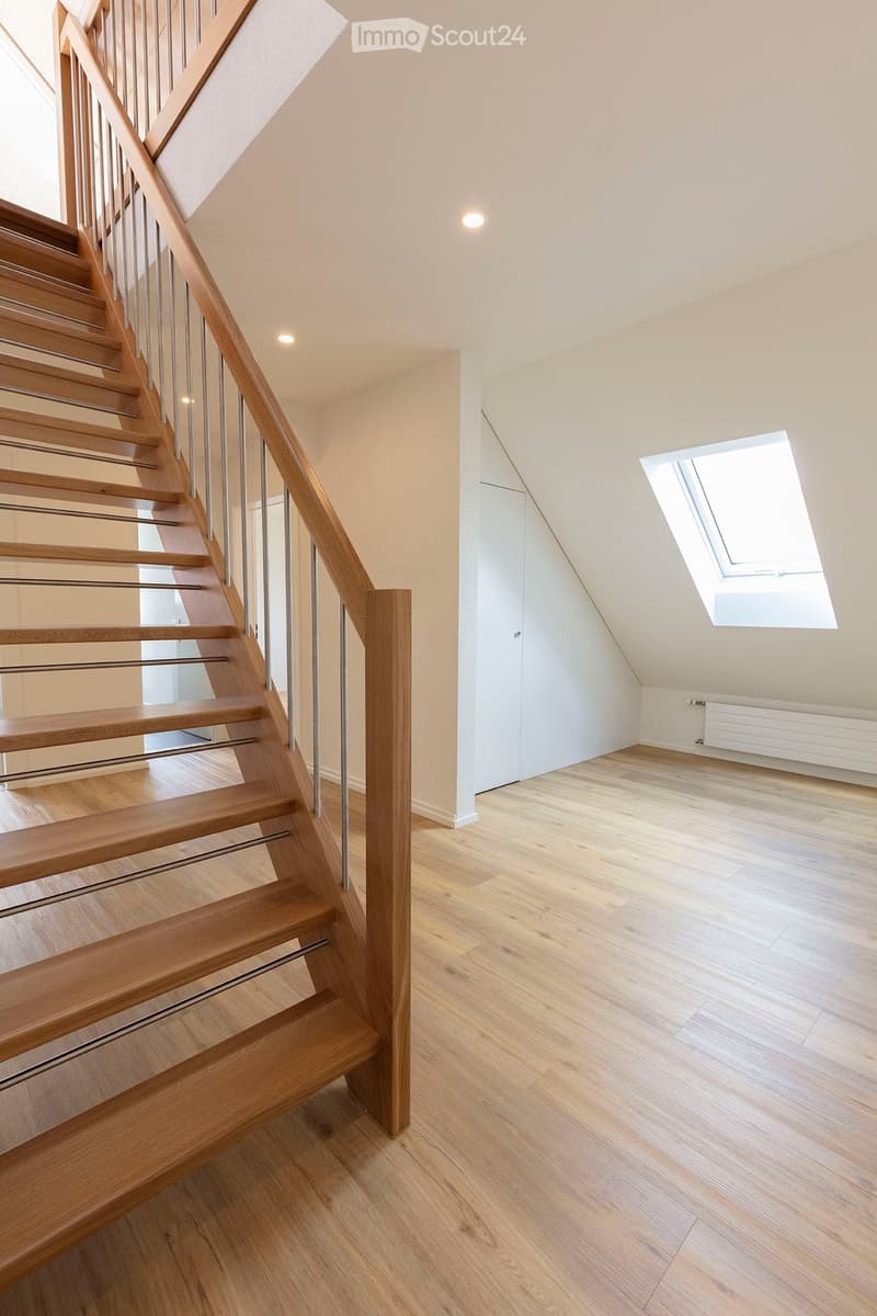Modern hallway with wooden staircase, light wooden flooring, white walls, and a skylight window at the end.