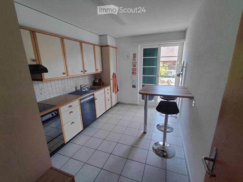 Modern kitchen with white cabinets, tiled floor, sink, oven, dishwasher, and a small dining area with a table and stools.
