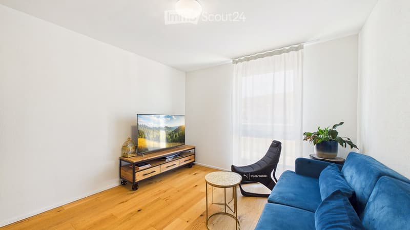 Modern living room with a blue sofa, coffee table, TV on a wooden stand, a single chair, and a small round table with a plant.