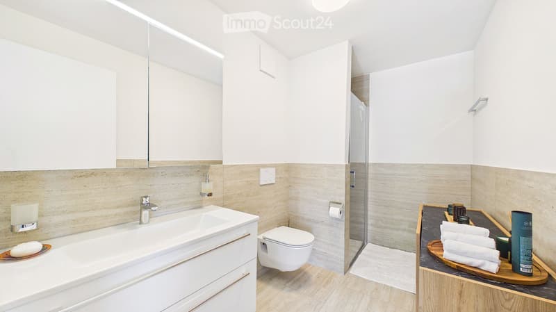 Modern bathroom with a white sink, toilet, large mirror, and a wooden tray with towels and toiletries.