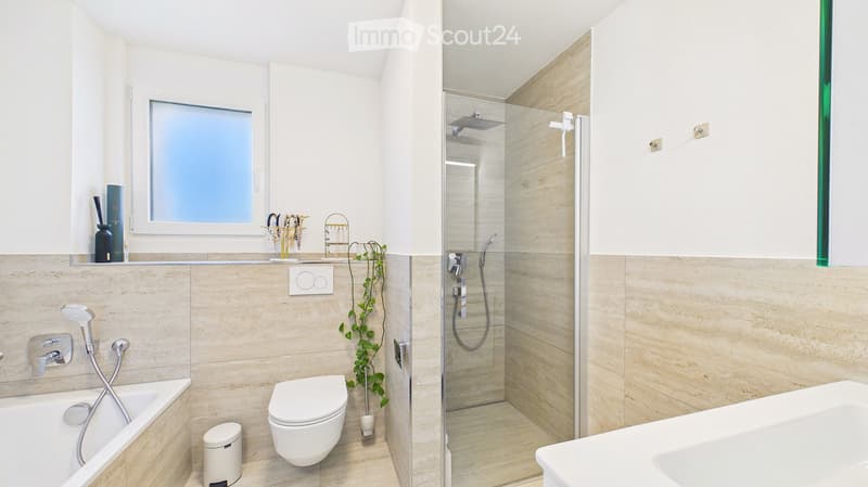 Modern bathroom with a bathtub, toilet, shower, and sink. Features a large window, decorative items on the windowsill, and a small plant in the corner.