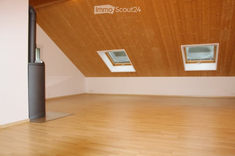 Empty room with wooden flooring and slanted wooden ceiling, featuring two skylight windows and a small black column.