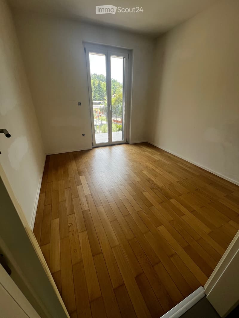 Empty room with wooden flooring, white walls, and a sliding glass door leading to a balcony.