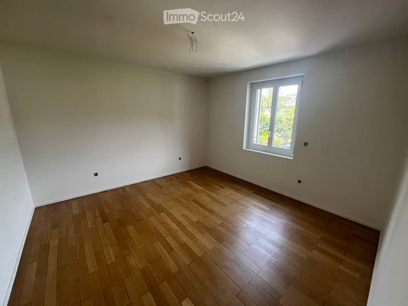 Empty room with wooden flooring and white walls, featuring a single window with white frame and visible outdoor view.