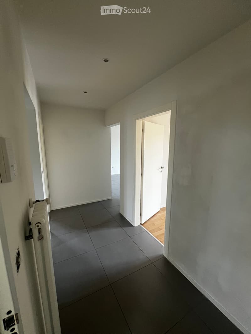 Empty hallway with grey tiled floor, white walls, and two open doors leading to other rooms.