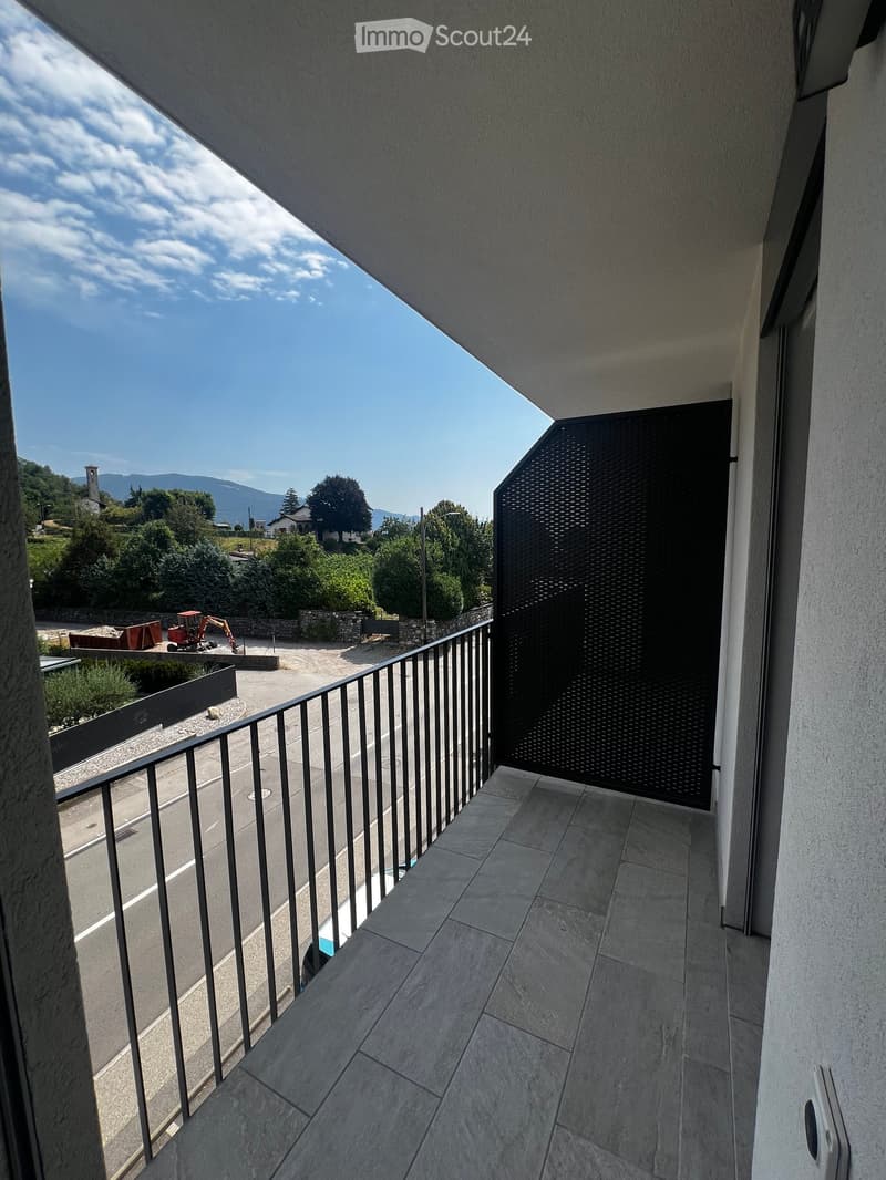 Balcony with tiled floor, metal railing, and a view of a road, trees, and distant mountains.