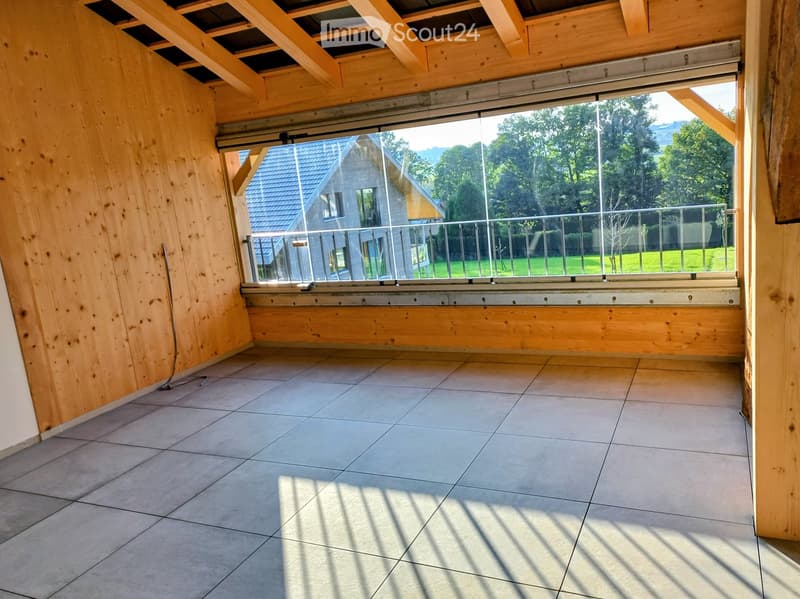 Empty room with wooden walls, tiled floor, and large window opening to a balcony with metal railing and outdoor view.