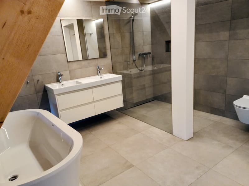Modern bathroom with a bathtub, double sink, mirror, toilet, and glass-enclosed shower area.