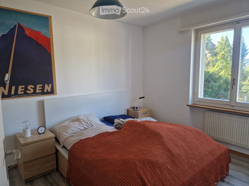 Cozy bedroom with a double bed, nightstands, a lamp, and a large window offering a view of greenery.