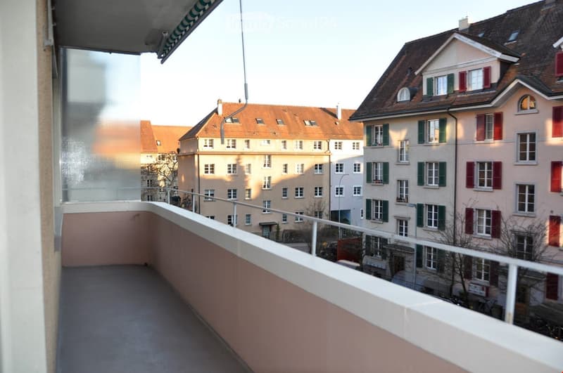 Balcony with a view of a residential area featuring multi-story buildings with red-tiled roofs and green shutters.