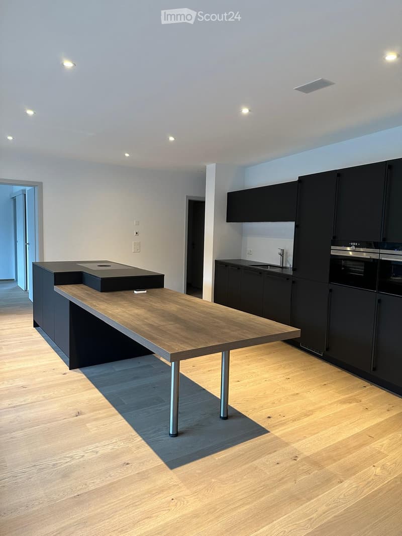 Modern kitchen with a wooden island, black cabinets, and stainless steel appliances.