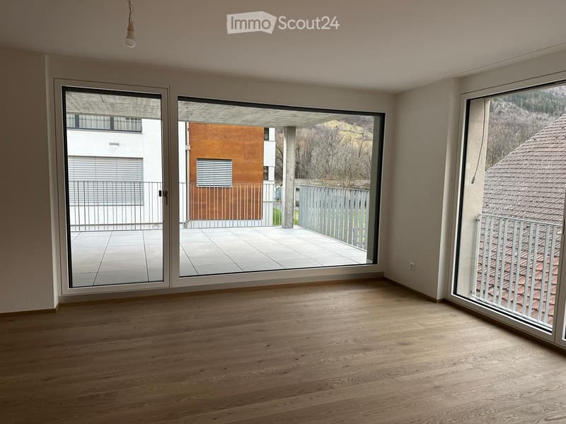 Empty room with wooden flooring, large sliding glass doors leading to a balcony, and a view of the surrounding area.