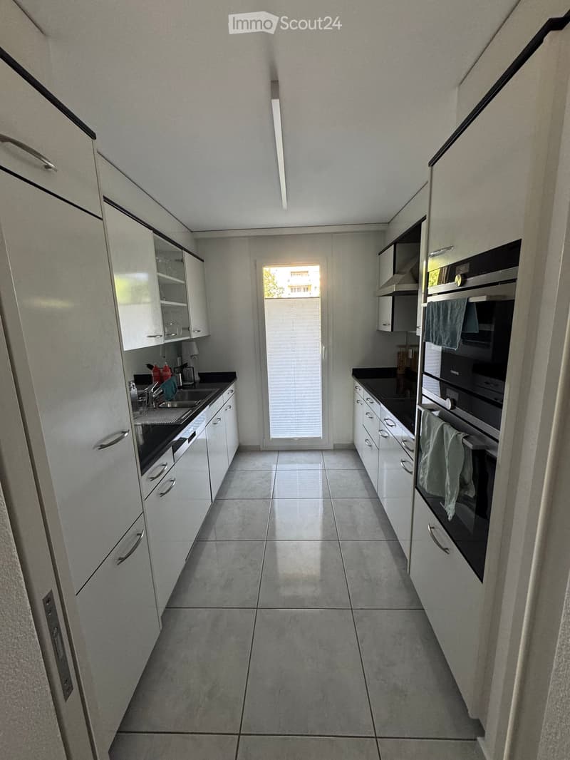 Modern kitchen with white cabinets, stainless steel appliances, and a large window with blinds.