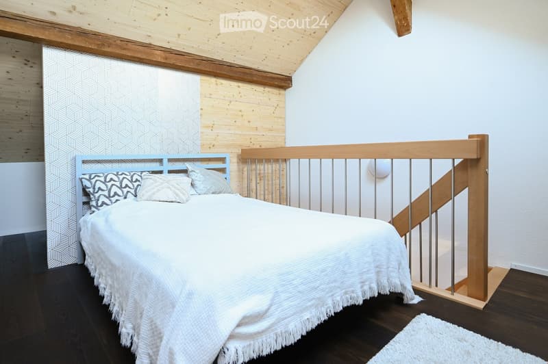 Cozy bedroom with a white bed, patterned pillows, a light blue headboard, and a wooden staircase railing in the background.