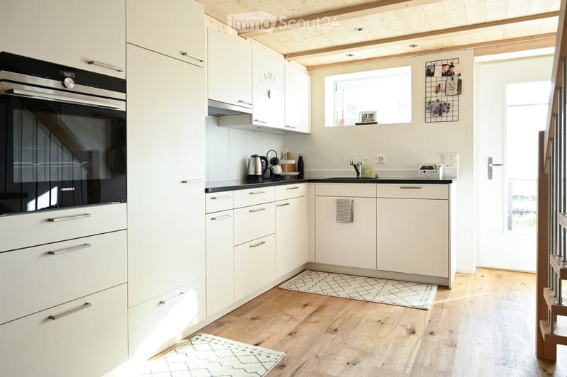Modern kitchen with white cabinets, stainless steel oven, wooden flooring, and small rugs.