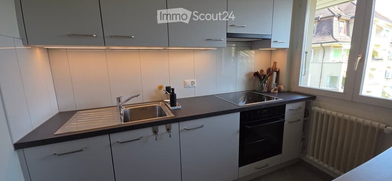 Modern kitchen with white cabinets, stainless steel sink, oven, and countertop. Features a window with a view of the street.
