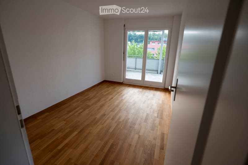 Empty room with wooden flooring, white walls, and large sliding glass doors leading to a balcony.