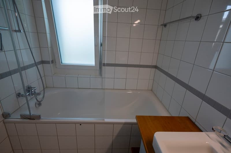 Modern bathroom with a bathtub, tiled walls, a wooden cabinet, and a sink.