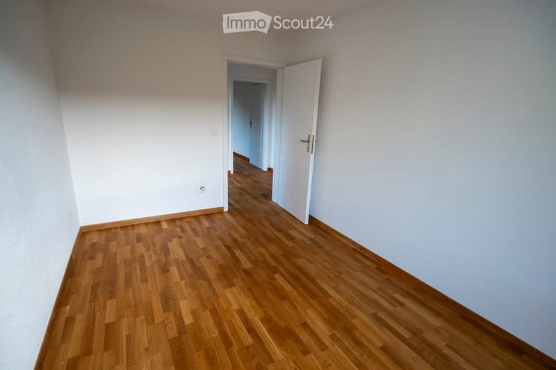 Empty room with light-colored walls and wooden flooring, featuring an open doorway leading to another room.