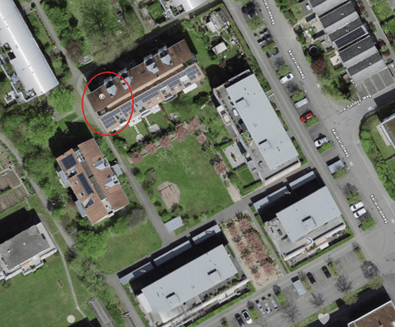 Aerial view of a residential area showing multiple houses with solar panels on their roofs, surrounded by greenery and streets.