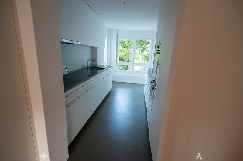 Empty kitchen area with white cabinets, stainless steel sink, and dark flooring. No furniture or appliances are present.