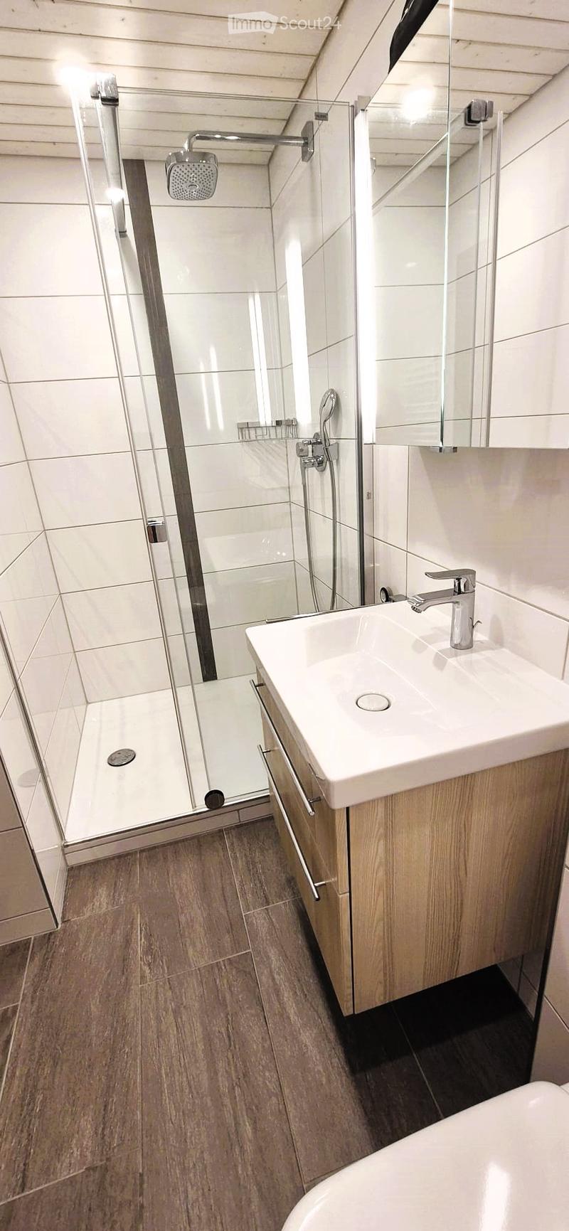 Modern bathroom with a white sink, chrome faucet, bathtub, glass-enclosed shower, and wooden cabinet.