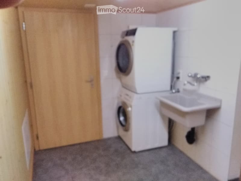 Bathroom with a washing machine, sink, and faucet.
