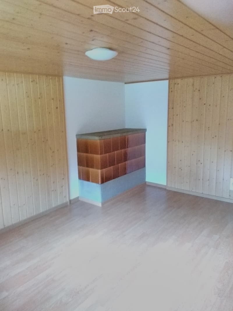 Empty room with wooden walls, light wooden floor, and a small brick and wood platform in the corner.