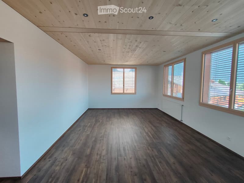 Empty room with wooden flooring, light blue walls, and wooden ceiling. Three windows with blinds are visible, allowing natural light to enter.