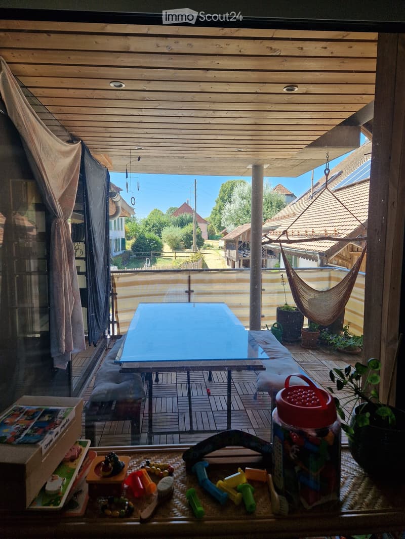 A wooden balcony with a table, chairs, a hammock, potted plants, and toys on a small table.