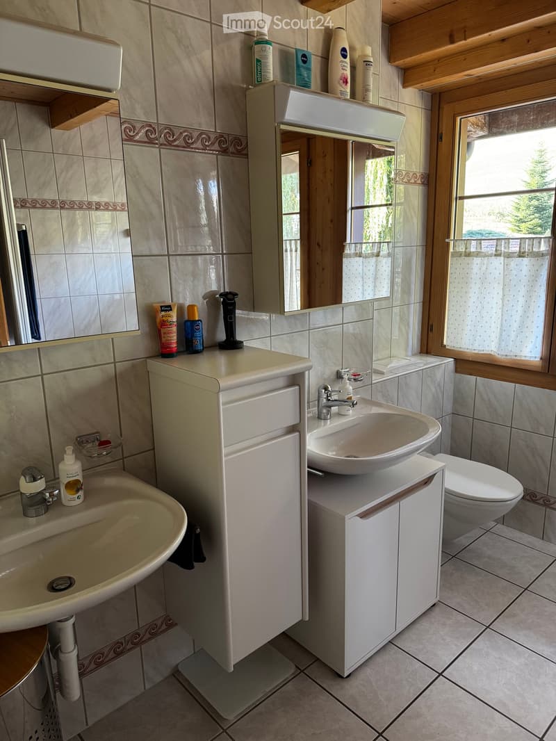 Bathroom with two sinks, a toilet, a mirror, and various toiletries on the counters.