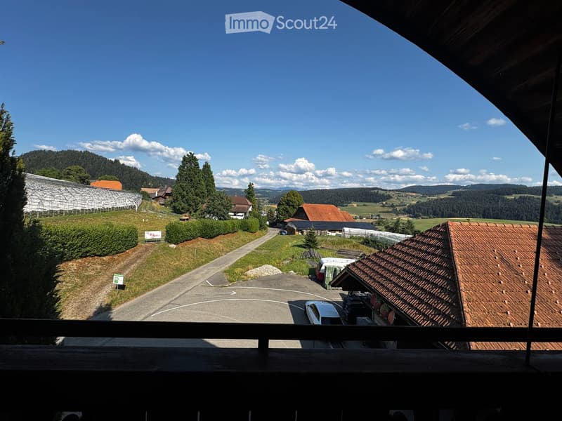 Balcony overlooking a rural landscape with houses, a greenhouse, and a parking area.