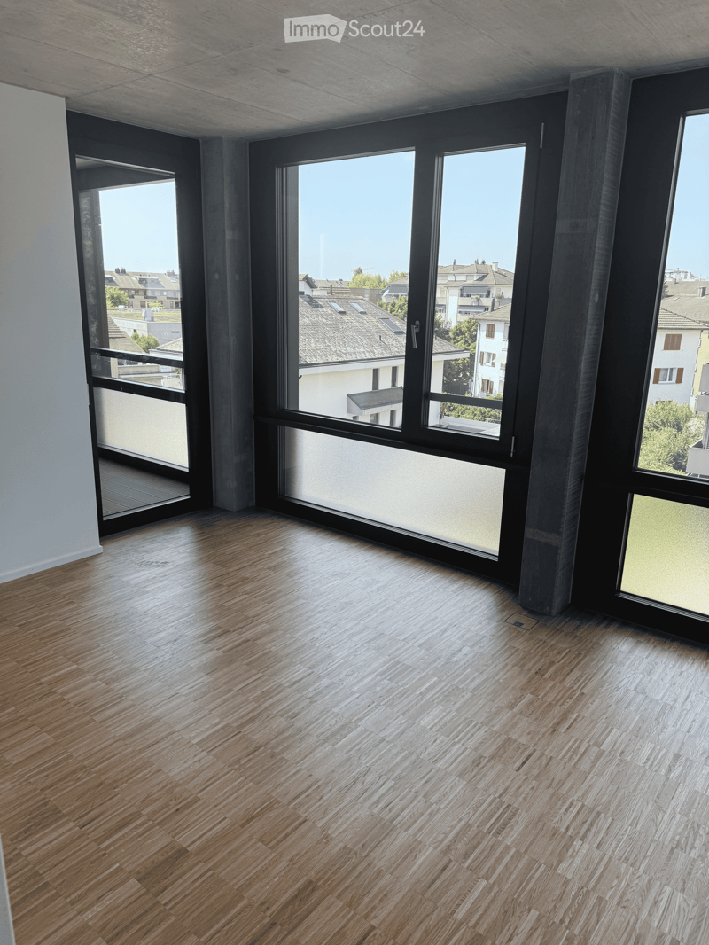 Empty room with wooden flooring and large windows offering a view of the neighborhood.