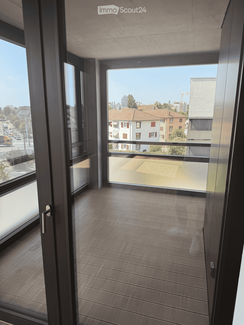 Modern balcony with wooden decking, large glass doors, and a view of the city and surrounding buildings.