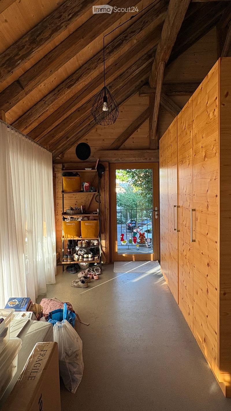 Wooden attic hallway with slanted ceilings, built-in shoe rack, and a large window leading to a balcony.